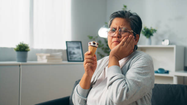 an elderly woman suffering from tooth sensitive after while holding an ice-cream